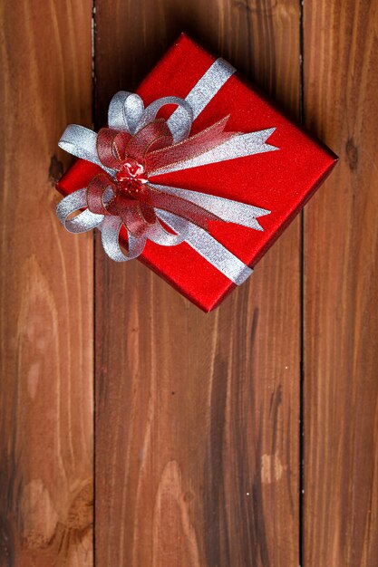 Vista superior de la pequeña caja de regalo envuelta en papel rojo con pajarita de cinta brillante plateada colocada en la vieja mesa de madera oscura en la fiesta de cumpleaños de la víspera de Navidad o festival de año nuevo.