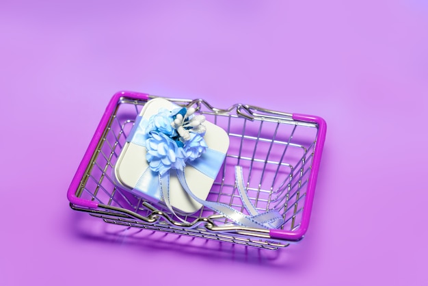 Vista superior de una pequeña cesta de la compra con una caja de regalo sobre un fondo rosa