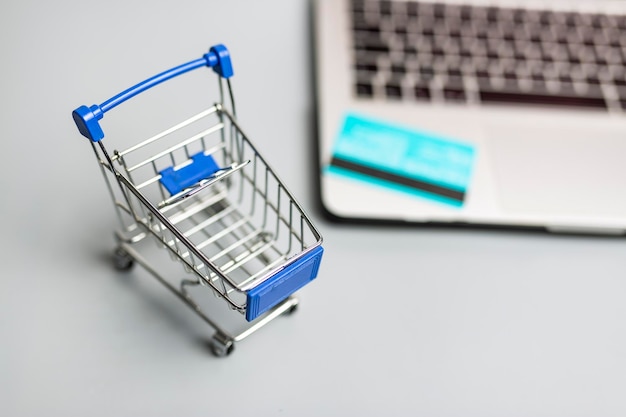 Vista superior de un pequeño carrito de compras con tarjeta de crédito sobre una computadora portátil borrosa en un fondo blanco