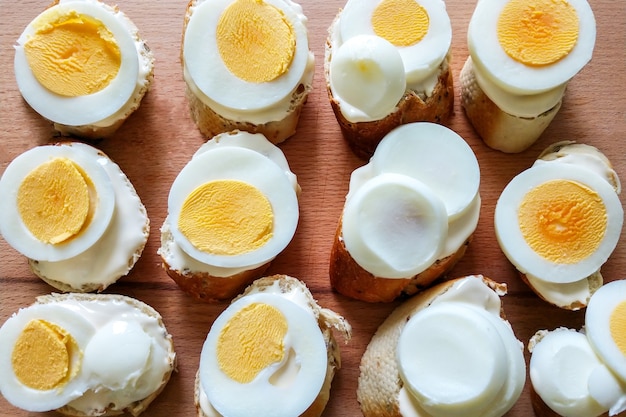 Vista superior de pequeños bocadillos de queso de pan blanco y huevos picados con yema sobre una tabla de madera