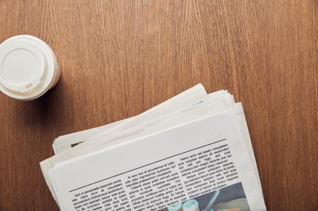 vista superior del periódico cerca de la taza de papel en la superficie de madera