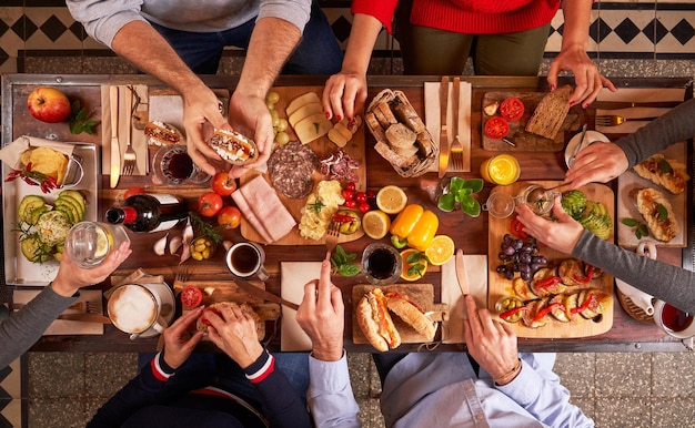 Vista superior de personas anónimas comiendo comida sabrosa mientras se sientan en una mesa de madera con aperitivos variados en una cocina ligera