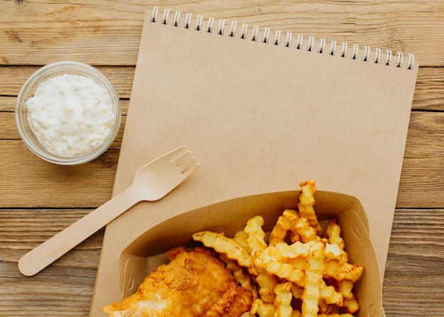 Vista superior de pescado y patatas fritas con salsa y cuaderno