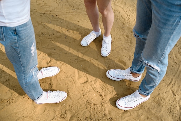 Vista superior de las piernas de los jóvenes en zapatillas blancas en la arena. Zapatos selfie desde arriba.