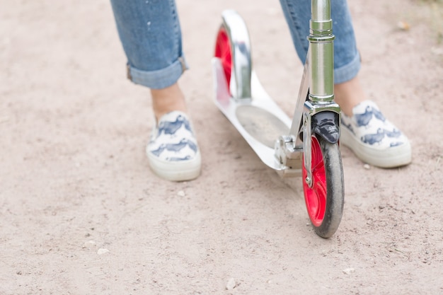 Foto vista superior de los pies de la mujer en zapatillas de deporte en el scooter en el parque