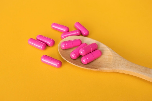 Vista superior de píldoras de vitaminas y minerales en una cuchara de madera en el espacio amarillo, producto de salud