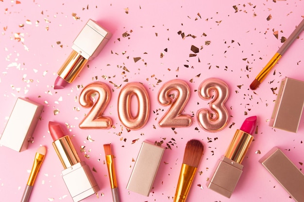 Vista superior de los pinceles cosméticos y lápiz labial sobre fondo rosa Números de oro rosa 2023