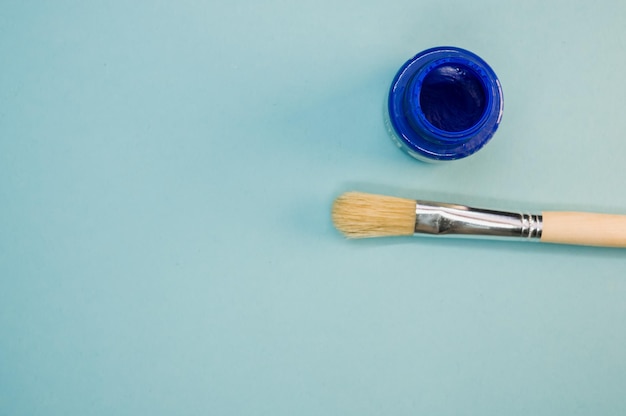 Vista superior de la pintura azul acrílica en la botella con un pincel en la superficie azul