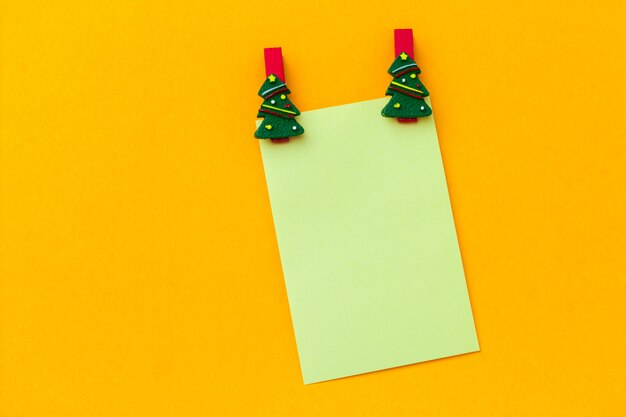 Vista superior pinzas festivas de Navidad y hoja de papel verde vacía con espacio libre para texto sobre un fondo amarillo vibrante