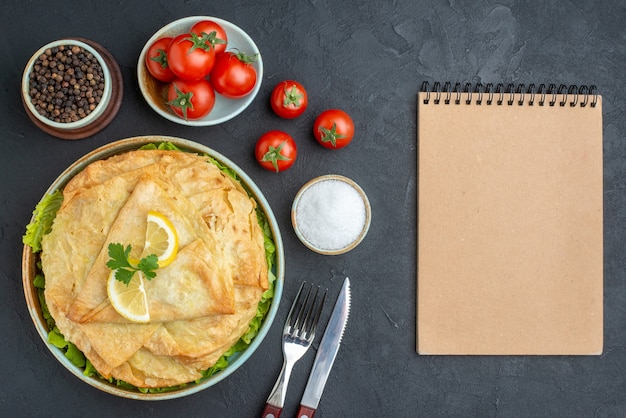 Vista superior pita cozida dentro do prato com rodelas de limão e tomate na superfície escura