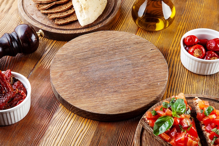 Foto vista superior placa de corte vazia para pizza ou carne. branches para servir comida em composição com tomates secos ao sol, bruschetta e utensílios em fundo de madeira. configuração plana