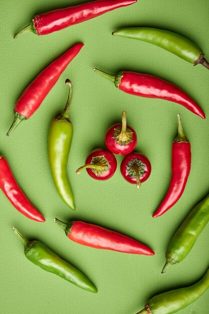 Vista superior plana de chiles rojos y verdes aislados sobre fondo verde acostado en el espacio de copia circular sobre el concepto de ver verduras