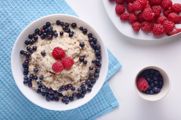 Vista superior plana de vegan breackfast caseiro, imagens de prato com aveia e frutas frescas frutas na mesa da cozinha branca, café da manhã na toalha azul na mesa. Alimentação saudável e conceito de cuidados de saúde.