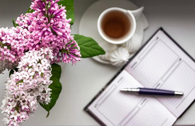 Vista superior plana con flores de color lila en un jarrón blanco en el alféizar de una ventana Bloc de notas para notas y una taza de café acogedora planificación de negocios en el hogar