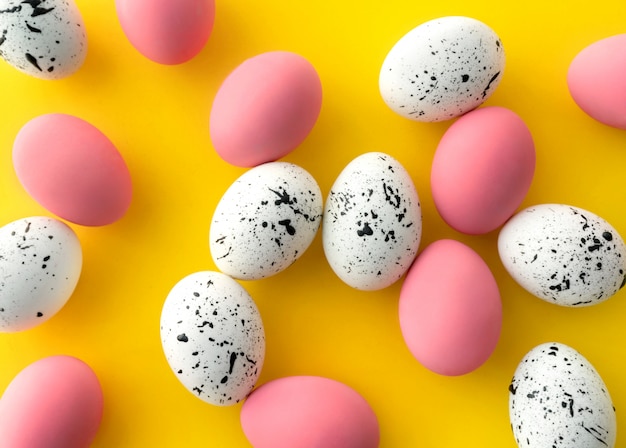 Vista superior plana de huevos blancos y rosados con diseños mínimos sobre fondo amarillo