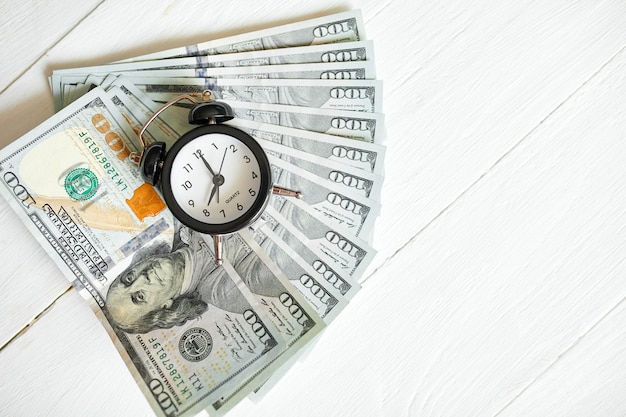 Vista superior plana lay do despertador e dinheiro em fundo branco de madeira, o tempo é o conceito de dinheiro
