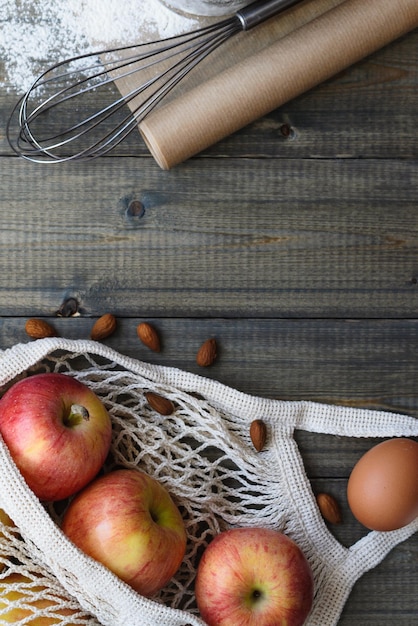 Vista superior plana na mesa de madeira com maçãs em saco ecológico e ovos e itens para assar