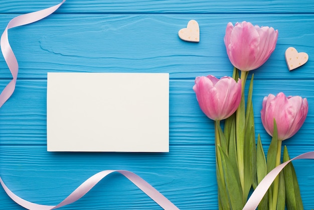 Vista superior plana vista aérea imagen fotográfica de hermosos tulipanes corazoncitos tarjeta de papel con espacio de maqueta en blanco vacío para el diseño de texto sobre fondo de escritorio brillante