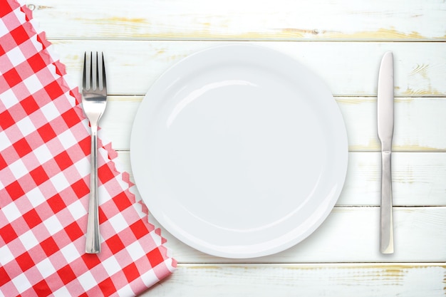 Vista superior de la plantilla de cocina italiana rústica de un plato blanco vacío con cubiertos en una mesa de madera