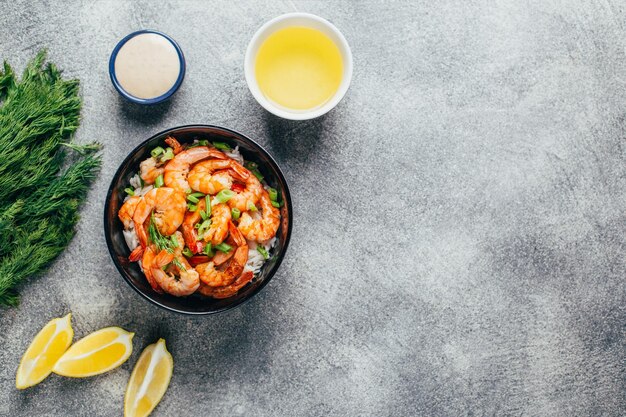 Vista superior de un plato de arroz y camarones en un plato al lado de salsa de hierbas y mantequilla sobre un fondo gris con espacio libre para texto