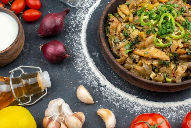 Vista superior del plato de berenjena servido con harina verde, especias, verduras, botella de aceite caída sobre fondo negro