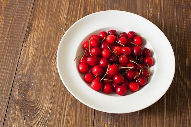 Vista superior del plato blanco con cerezas rojas frescas en la mesa de madera marrón