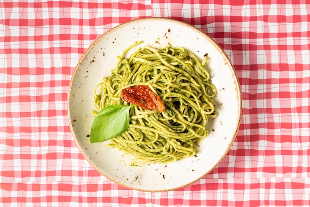 Vista superior de un plato de espaguetis con salsa pesto sobre un mantel a cuadros rojo y blanco