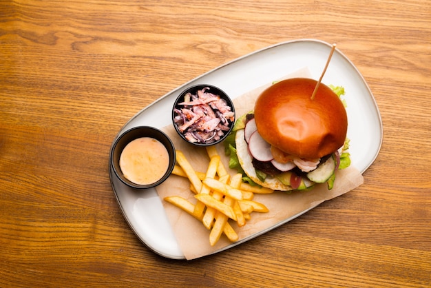 Vista superior de un plato con una hamburguesa y unas patatas fritas y salsa.