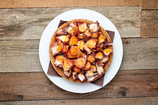 Vista superior de un plato de pulpo con aceite de oliva y pimentón aislado en una mesa de madera