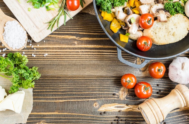 Vista superior de un plato en una sartén junto a los ingredientes de la tienda de comestibles en una mesa de madera