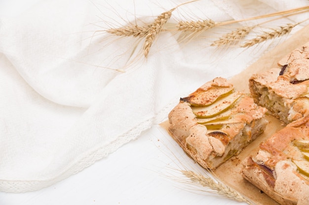 Vista superior en el plato con tarta de manzana crujiente casera con textiles blancos y orejas doradas de centeno