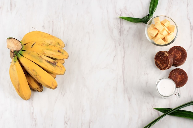 Vista superior Preparação de ingredientes fazendo Compota de Banana e Batata Doce (Kolak Pisang Ubi). Banana Madura, Batata Doce, Açúcar de Palma (Gula Merah), Folhas de Pandan e Leite de Coco. Popular para o Ramadã