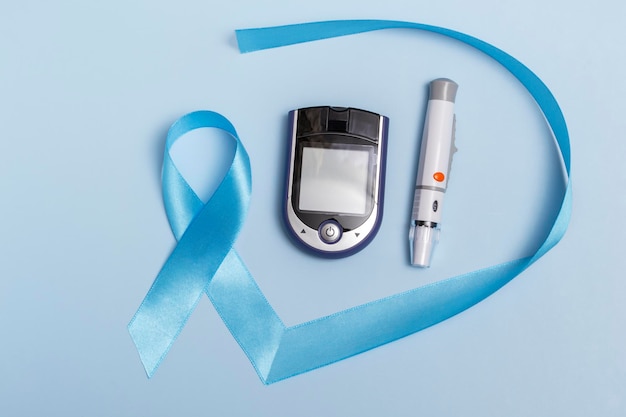 Vista superior de primer plano del concepto del Día Mundial de la Diabetes del 14 de noviembre. Cinta azul con gotas de sangre y un glucómetro sobre un fondo azul. Copia espacio