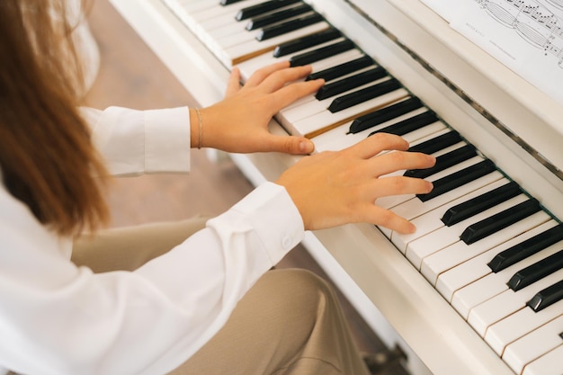 Vista superior de primer plano de una pianista irreconocible que toca música suave en un piano clásico blanco en un aula ligera