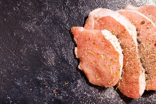 Vista superior de primer plano sobre carne cruda sazonada con especias, pimienta y sal sobre tabla de madera oscura