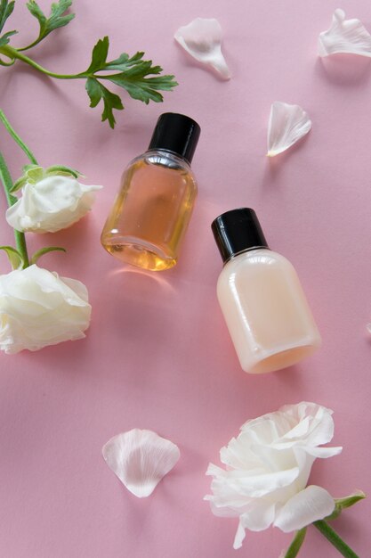 Vista superior de productos cosméticos y delicadas flores sobre fondo rosa. Tratamiento de belleza de bienestar. Productos orgánicos para el cuidado de la piel