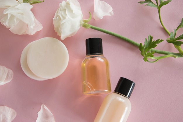 Vista superior de productos cosméticos y delicadas flores sobre fondo rosa. Tratamiento de belleza de bienestar. Productos orgánicos para el cuidado de la piel