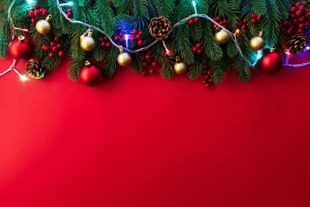 Vista superior de las ramas de abeto de Navidad, piñas, frutos rojos y campana sobre fondo rojo.