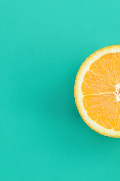 Vista superior de una rebanada de fruta de una naranja sobre fondo brillante en color verde turquesa