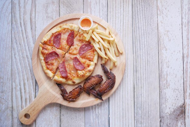 Vista superior de una rebanada de pizza de pollo y papas fritas en la mesa una tabla de madera en la mesa