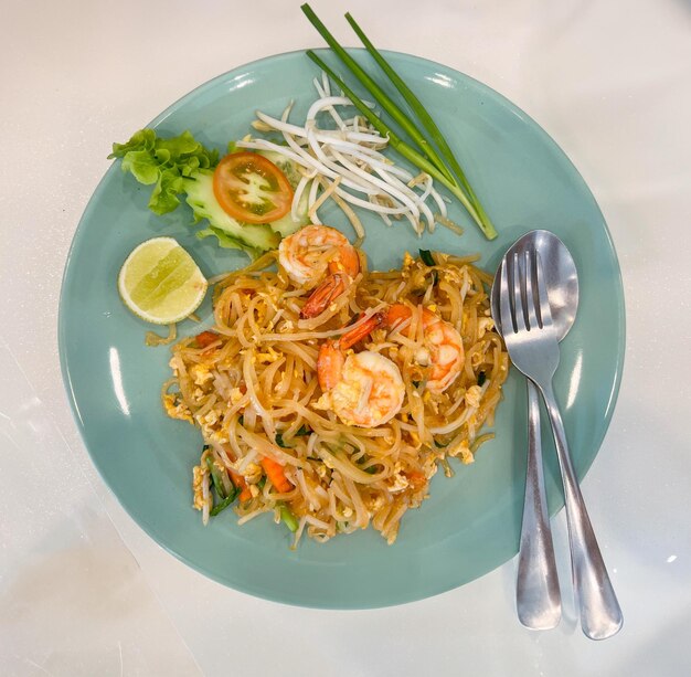 Vista superior de la receta tailandesa recién cocinada y salteada de fideos tailandeses con gambas en un plato redondo de cerámica