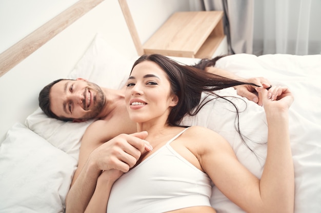 Vista superior de los recién casados complacidos posando en la cama para el frente