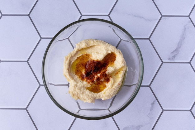 Vista superior de un recipiente de vidrio con hunmus de garbanzos decorado con pimentón y aceite de oliva.