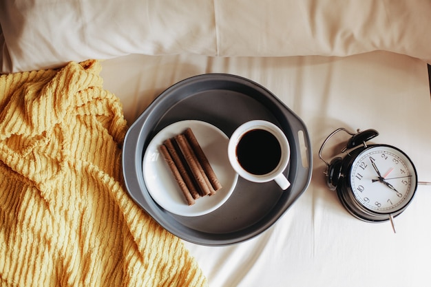 Vista superior de un refrigerio y una taza de café para el desayuno con reloj que muestra las 7 en punto en la cama