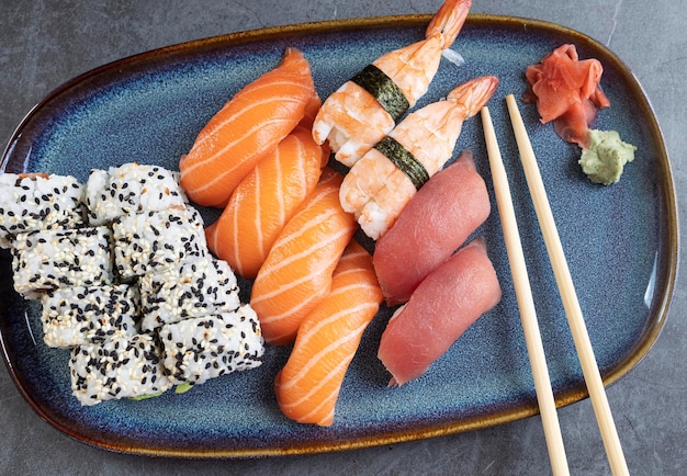 Vista superior de rollos de sushi clásicos con nigiris de salmón, wasabi, jengibre y palillos