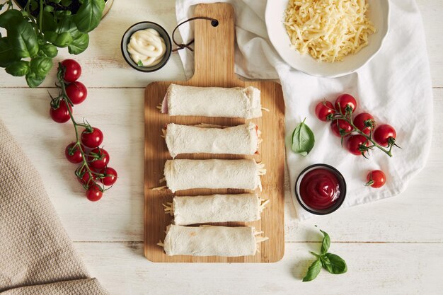 Vista superior de rollos de tostadas de jamón crudo y queso en un tablero sobre la mesa con ingredientes en él