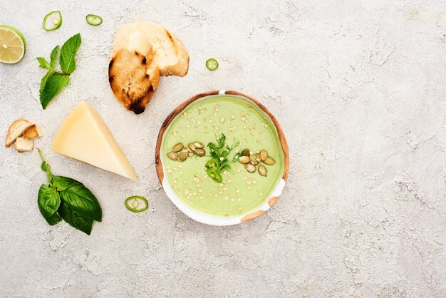 Foto vista superior de una sabrosa sopa cremosa verde en un cuenco con croutons en un fondo gris texturizado