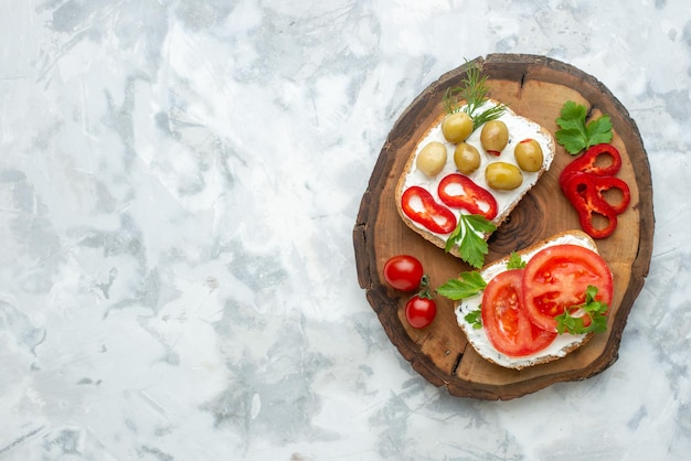 Vista superior sabrosas tostadas con tomates y aceitunas en la superficie blanca de la tabla de madera