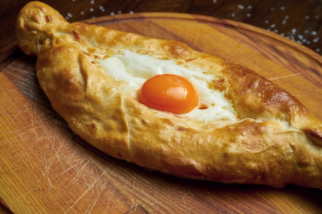 Vista superior de sabrosos Khachapuri Adjarian tradicionales - pastel abierto al horno con queso salado derretido (suluguni) y yema de huevo en bandeja de madera. Comida tradicional georgiana