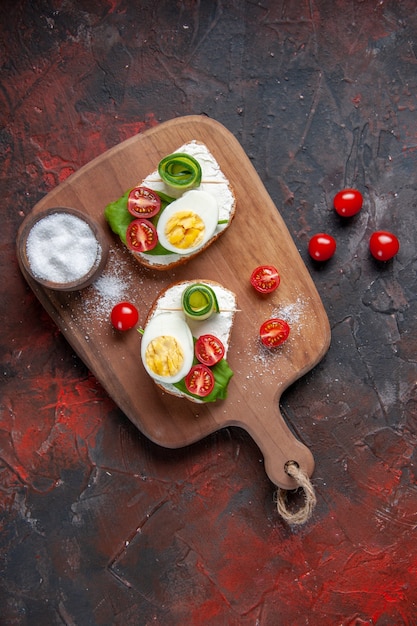 Vista superior sabrosos sándwiches de huevo con tomates rojos sobre tabla de cortar fondo rojo oscuro sándwich comida pan comida hamburguesa bocadillo tostadas